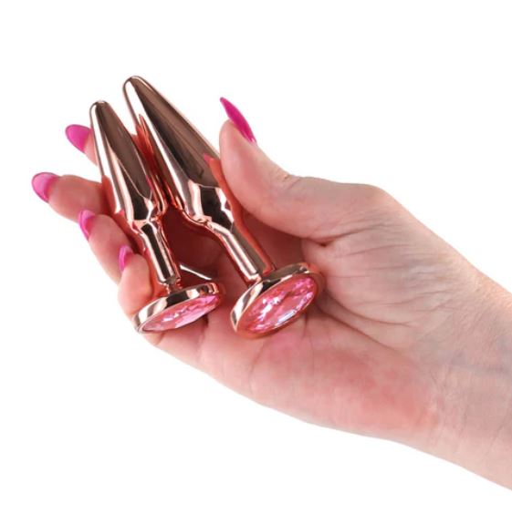Rear Assets Tapered Trainer Chrome Plated Anal Plugs Kit Rose Gold in a hand, showcasing luxurious design and colors.