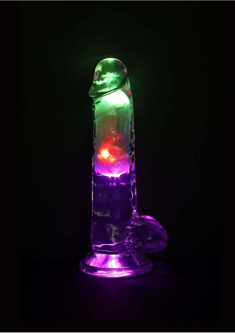 RealRock Vibrating Dildo 7 inch with Balls and Remote Control, illuminated in vibrant colors against a dark background.