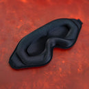 Sei Mio Total Eclipse Deluxe Blackout Mask on a textured orange background, showcasing its contoured design and soft padding.