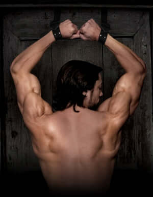 Man with muscular back bound in Command Bondage Door Cuffs, showcasing strength and restraint for BDSM enthusiasts.
