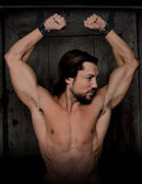 Man with muscular build restrained in door cuffs, showcasing BDSM bondage setup with industrial strength straps.