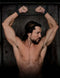 Man with muscular build restrained in door cuffs, showcasing BDSM bondage setup with industrial strength straps.