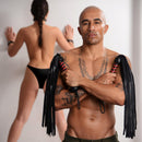 The model showcases a Strict Leather Bullhide Flogger, emphasizing its deep, thuddy impact in an intimate setting.