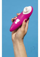 Hand holding We-Vibe ROMP Shine clitoral stimulator in pink and white.