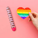 Pride Vibe Pink from Blush Novelties beside a hand holding a rainbow heart on a pink background