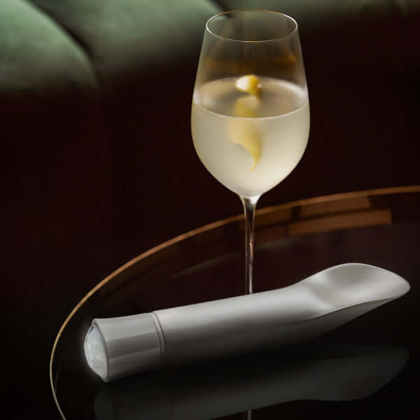 Oh My Gem Bold Diamond Silver Vibrator by Blush Novelties next to a glass of white wine on a table.