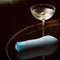 Oh My Gem Ardor Aquamarine Blue Rechargeable Vibrator next to a martini glass with an olive on a glossy black table.