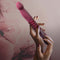 Woman holding the Temptasia Trixie Thrusting Dildo from Blush Novelties in a floral background.