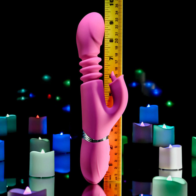 Pink Dragon Rabbit Vibrator displayed next to a ruler, set against a background of colorful candles.