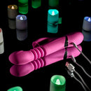 Pink Dragon Rabbit Vibrator on a reflective surface surrounded by colorful LED candles, showcasing its USB charging feature.