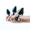 Hand holding three chrome-plated, rainbow-colored anal plugs from Rear Assets Rainbow Heart Trainer Kit.
