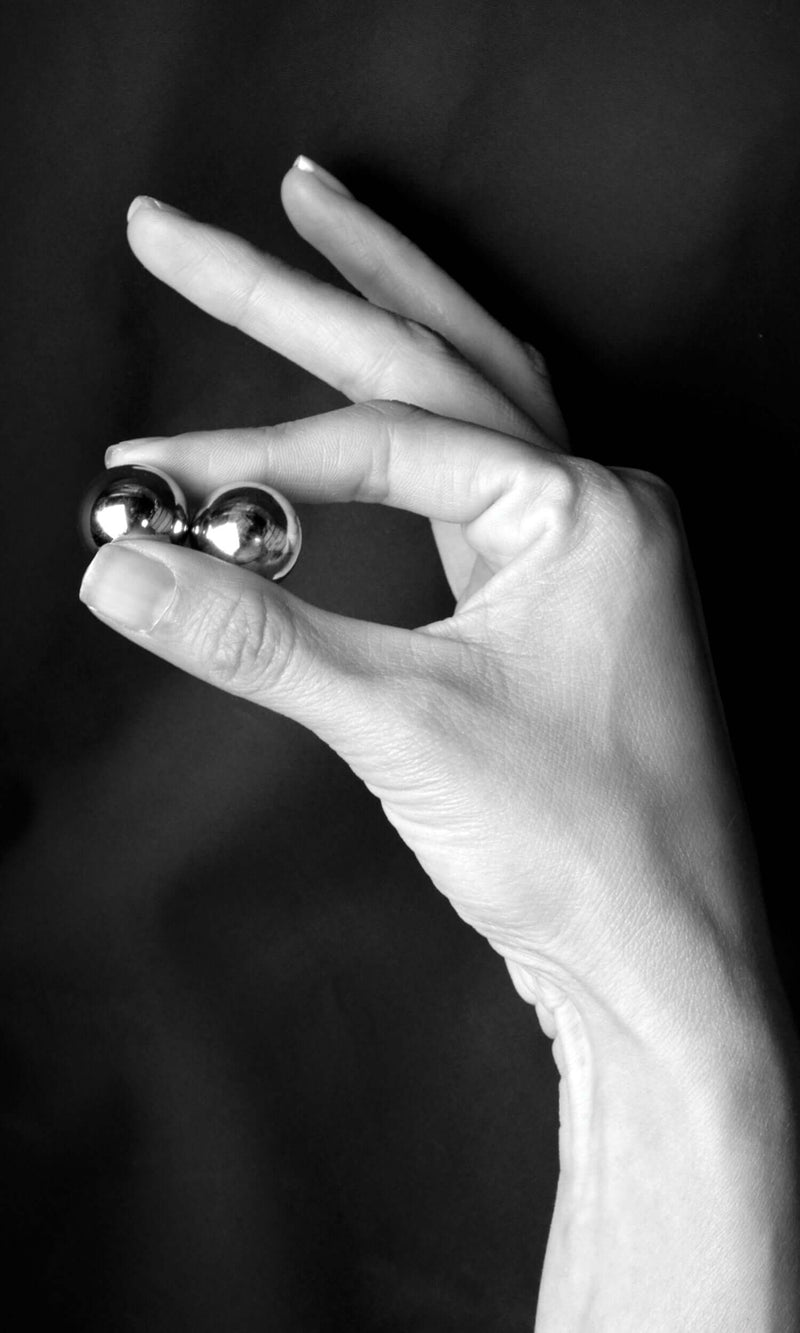 Hand holding Fetish Fantasy Limited Edition Ben Wa Balls Gold against black background