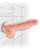 King Cock Triple Density 9-inch beige dildo with balls attached to a tiled wall, featuring realistic details and a strong suction cup.