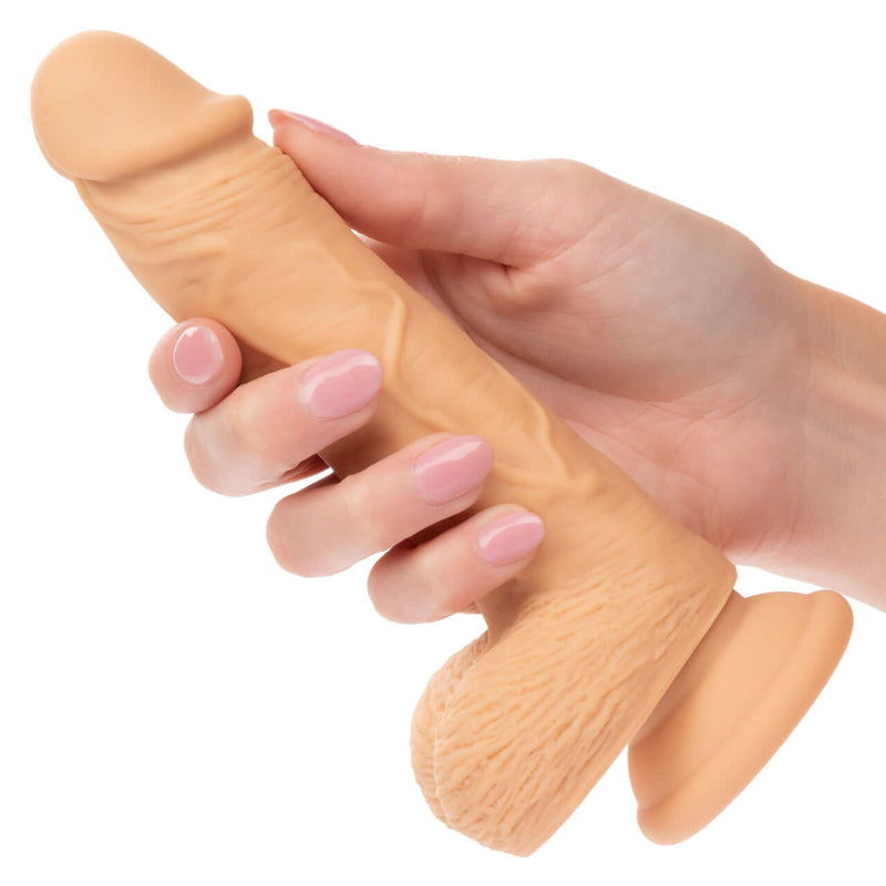 Hand holding 5-inch Dual Density Silicone Stud Dildo with suction cup base in light ivory skin tone from California Exotic Novelties.