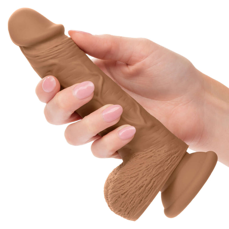 Hand holding Dual Density Silicone Stud Dildo 5 inches Brown with suction cup base.