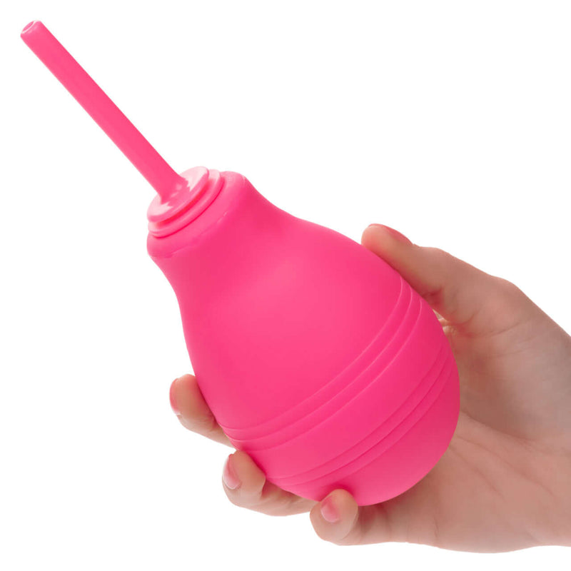 A hand holding a pink Cheeky One Way Flow Douche featuring a slender nozzle for intimate hygiene and comfort.