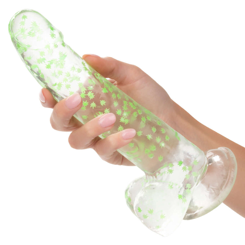 Hand holding Naughty Bits I Leaf Dick Glow In The Dark Weed Leaf Dildo with suction cup base and glow in the dark weed leaf design.