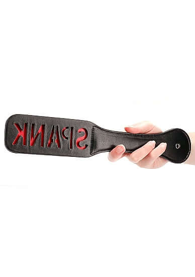 Hand holding the Paddle Spank Black with reversed 'SPANK' imprint, made from durable faux leather.