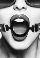 Black and white image of a person wearing a silicone ring gag with adjustable straps, emphasizing bondage aesthetics.