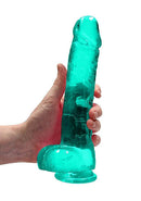 Hand holding Realrock 9-inch turquoise green dildo with balls by Shots Toys America, featuring a lifelike crystal clear design.