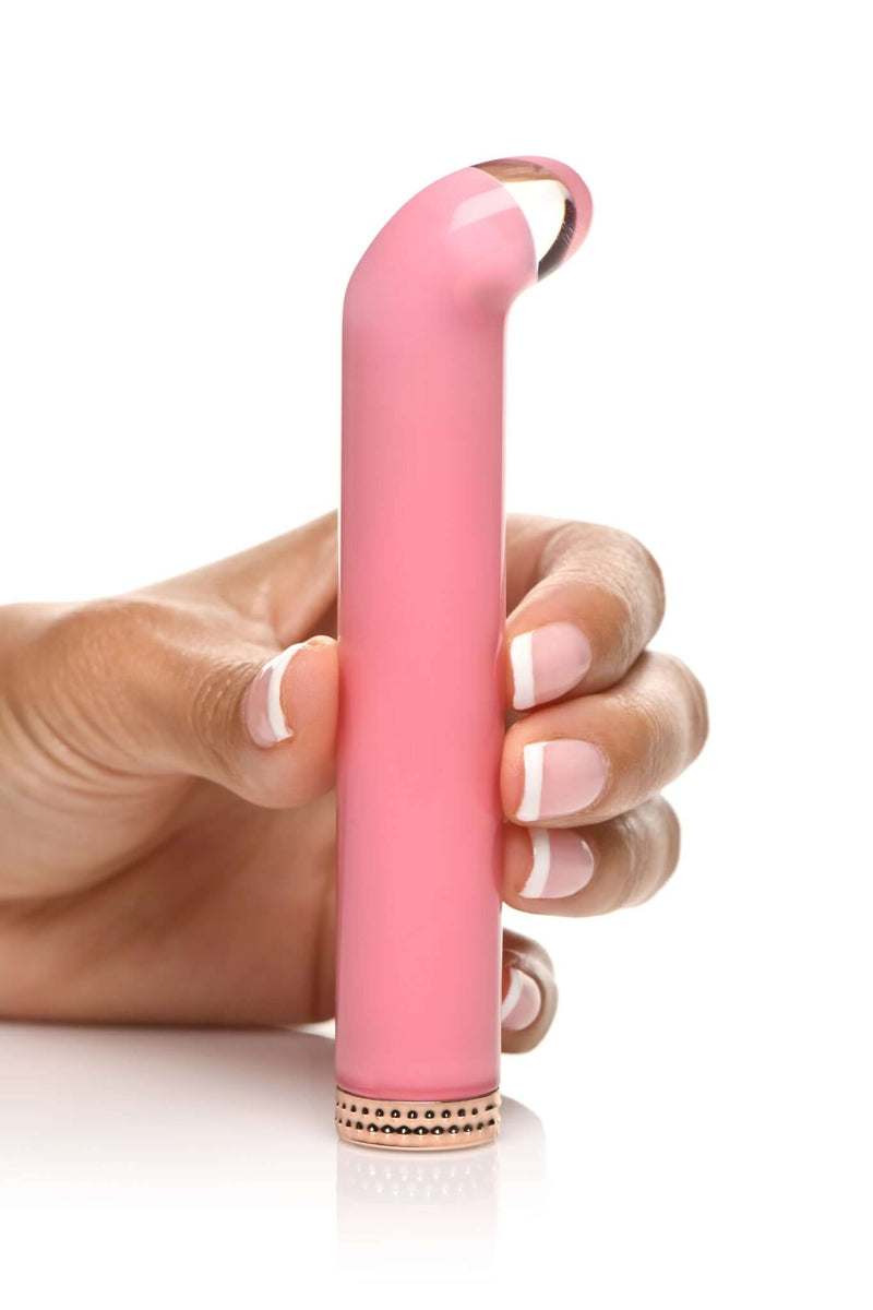 Person holding the Prisms Vibra Glass 10X G-Spot Vibrator in Pink with a golden ring base from XR Brands.