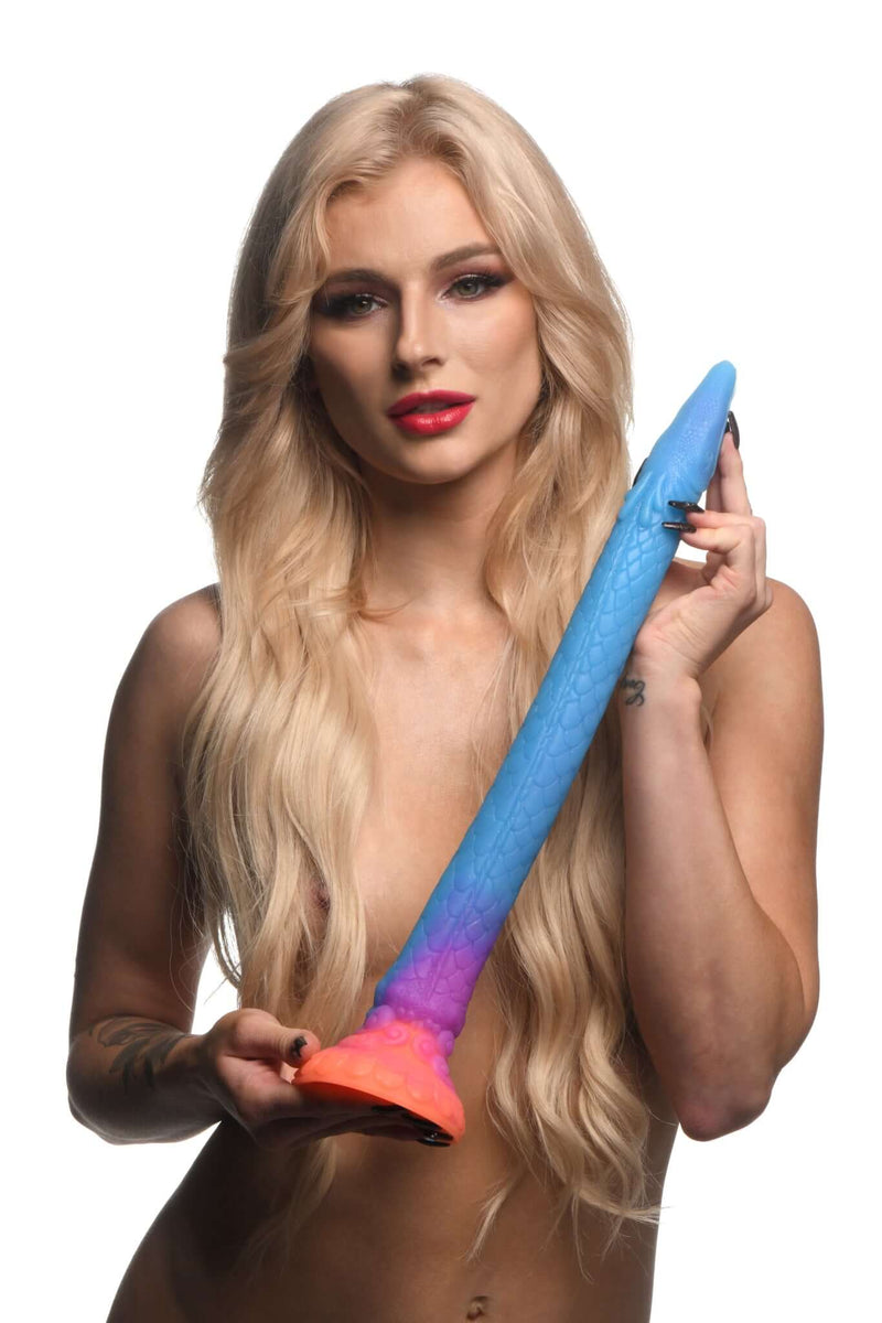 Model holding 16-inch Makara Glow In The Dark Silicone Snake Dildo by Creature Cocks in blue and orange gradient colors.