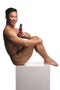 Smiling person holding Creature Cocks Hell Kiss Twisted Silicone Dildo from XR Brands, sitting on a white cube.